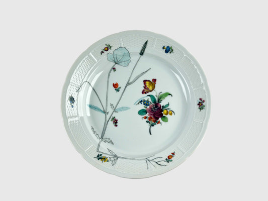 Runde Platte mit leicht gewelltem Rand und feiner Korbrelief-Struktur. Die Mitte ziert ein farbenfrohes Blumenbouquet, ergänzt durch feine botanische Zeichnungen in Schwarz. Der Tellerrand ist mit kleinen, farbigen Blüten und Insekten dekoriert.

Round porcelain platter with a gently scalloped edge and fine basket-weave relief. The center features a colorful floral bouquet, complemented by delicate black botanical line drawings. The rim is adorned with small, colorful flowers and insects.